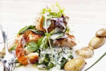 Salmon filet with scampi on a bed of spinach with potatoes in their skins and creamy wine sauce