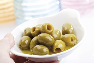 Hand holding green olives in small porcelain bowls