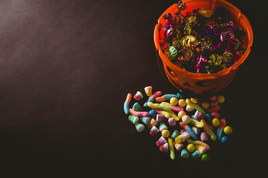 Candies by bucket with wrapped chocolate over black background