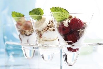 Muesli with yoghurt in a small glass jar, raspberries, sliced banana, grapes, mint leafs