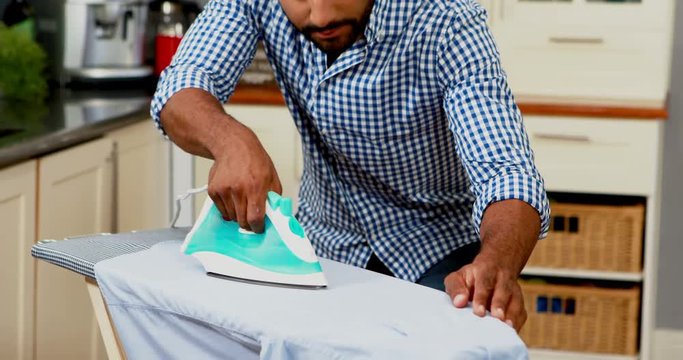 Mid section of man ironing clothes in kitchen 