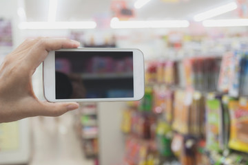 Woman hand holding smart phone in super market shopping blur background.