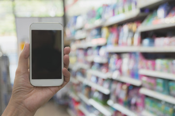 Fototapeta na wymiar Woman hand holding smart phone in super market shopping blur background.