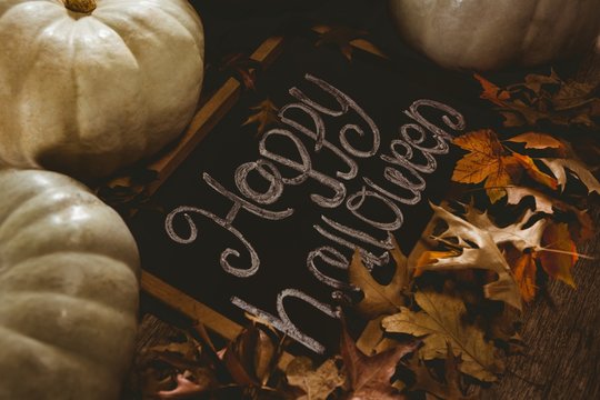 View of happy Halloween text on slate with pumpkins and autumn