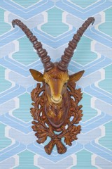 Fototapeta premium Plastic head of an ibex mounted on kitschy wallpaper from the 1960s or 1970s, frontal view