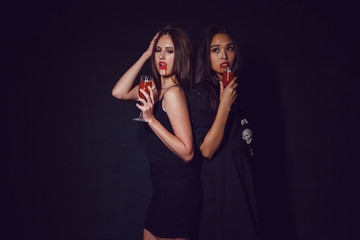Fototapeta na wymiar Attractive girls in the image of vampires hold glasses with blood. Halloween.