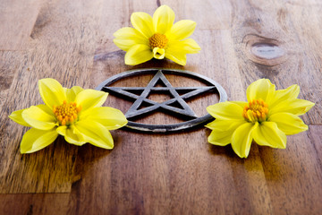 Fototapeta na wymiar Metal pentagram with yellow dahlia flowers on wooden background