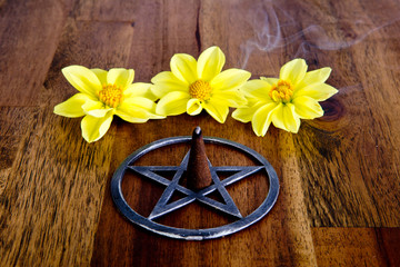 Burning incense in metal pentagram with yellow dahlia flowers on wooden background