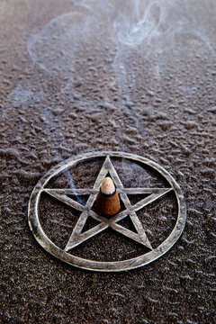 Burning incense in center of gray metal pentagram on slate background with water drops