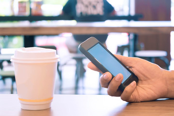 Closing businesswoman hand using smartphone in coffee shop with white paper cup of hot coffee, Business Technology and Ordering Food Online Concept