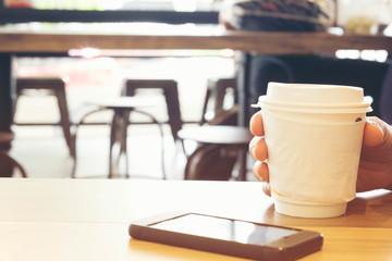 Closing businesswoman hand using smartphone in coffee shop with white paper cup of hot coffee, Business Technology and Ordering Food Online Concept