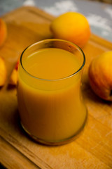 Glass of peach juice with fresh peaches on the rustic background. Shallow depth of field.