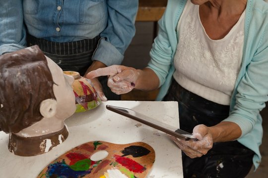 Woman using digital tablet while painting a sculptor