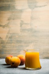 Glass of peach juice with fresh peaches on the rustic background. Shallow depth of field.