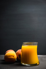 Glass of peach juice with fresh peaches on the rustic background. Shallow depth of field.