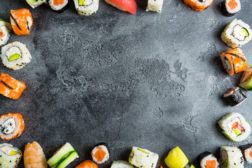 Frame with set of traditional japanese food on a dark background. Sushi rolls, nigiri, raw salmon steak, rice, and avocado. Flat lay. Top view