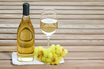 Bottle and glass of white wine are stand on table together grapes
