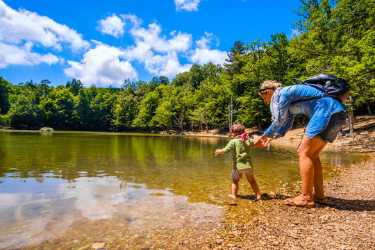 mother help baby to enter with feet in lake waters during a family trip in the nature of Foresta Umbra - Gargano Apulia - Italy