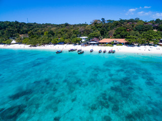Aerial top view of tropical island with white beach and blue transparent water. Snorkeling people near wooden longtail boats above coral reef. Phi-Phi Don Island, Thailand.