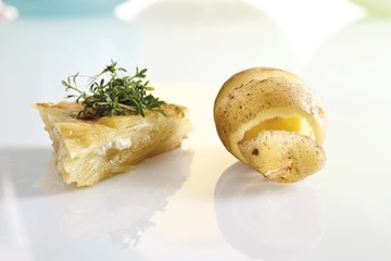 Slice of potato casserole with cress and a raw potato with a spiral of peel