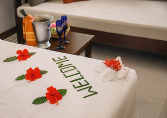 Word WELCOME and beautiful flowers on bed in hotel room