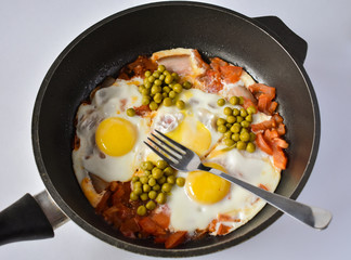 Eggs with tomatoes and green peas in a frying pan