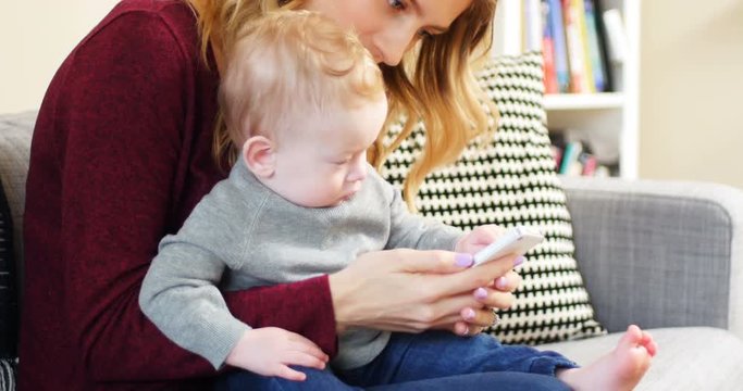 Mother and baby using mobile phone on sofa 