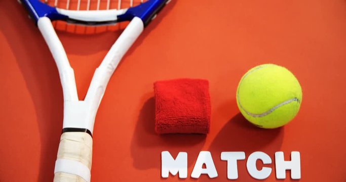 Close-up of tennis ball, wrist band and racket on red floor 