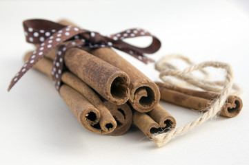 Fresh raw cinnamon sticks on white background tied with brown dotted bow and jute rope