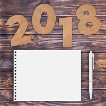 Cardstock Numbers 2018 Happy New Year Sign near White Spiral Paper Cover Notebook with Pen over table. 3d Rendering