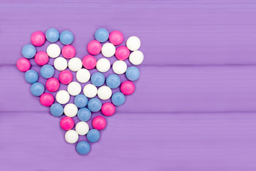 Candies of different colors forming a heart on a purple background