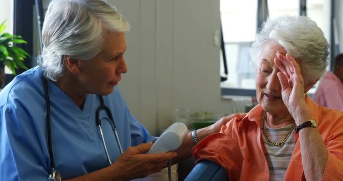 Female doctor checking blood pressure of senior woman 