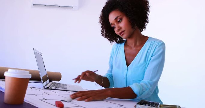 Female architect working on blueprint over drafting table 