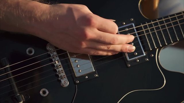 Close-up shot of a man plying solo guitar in music band. View to the hand plucking fingerboard