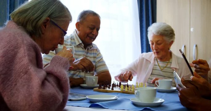 Mixed-race senior citizens using mobile phone and digital tablet while playing chess 