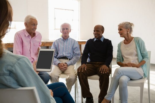 Woman holding tablet computer while discussing with senior