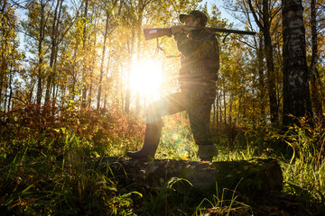 A hunter with a gun in the forest at dawn.
