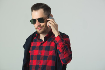 handsome young guy in a plaid shirt in sunglasses in the studio on a wall background talking on the phone