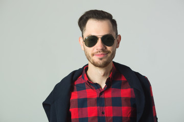 handsome young guy in plaid shirt in sunglasses in studio on wall background