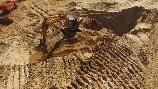 Excavator digging works in a quarry heavy equipment mining. Orange sand soil rock heavy industry. Aerial drone action flight close. Sunny day.