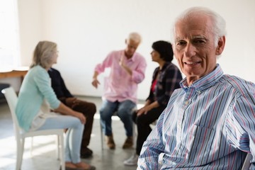 Portrait of senior man sitting on chair with friends discussing