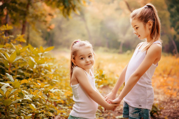 Childhood, family, friendship and people concept - two happy kids sisters hugging outdoors.