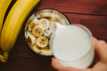 Pouring milk in blender over pieces of bananas, banana smoothie, top view