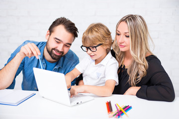 happy cute little school boy in glasses doing homework with parents