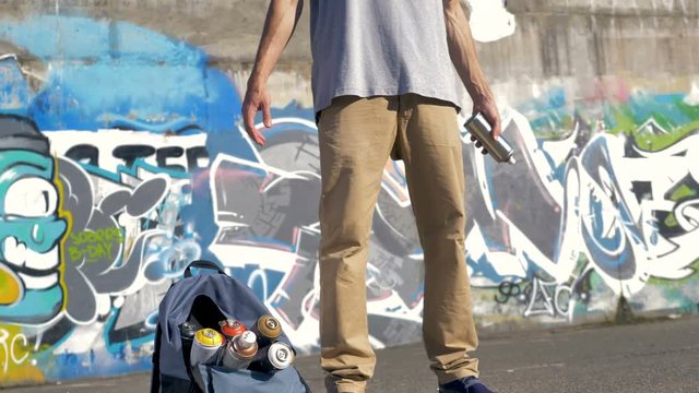 A male graffiti artist throws a paint can between his hands.