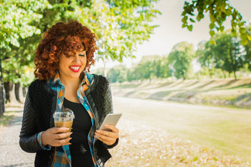 Cute curly redhead girl with smart phone and takeaway coffee