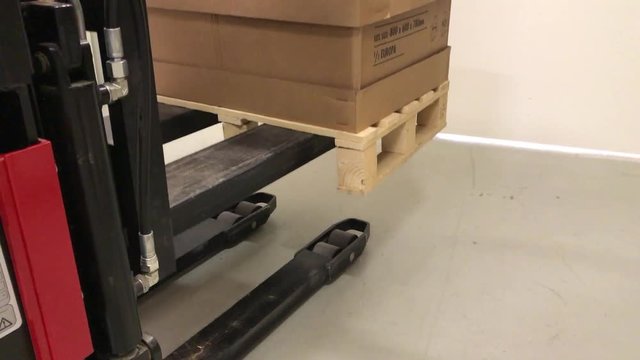 Industrial forklift lifting up pallet from ground.