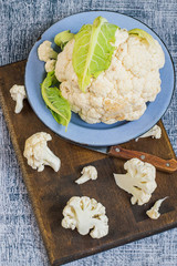   Fresh cauliflower in a metal bowl and on a kitchen cutting board on an old wooden table. The concept of healthy eating. Top view.