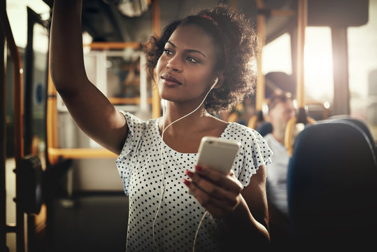 Young African woman riding on a bus listening to music