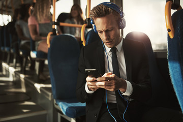 Businessman wearing headphones and reading text messages on a bus
